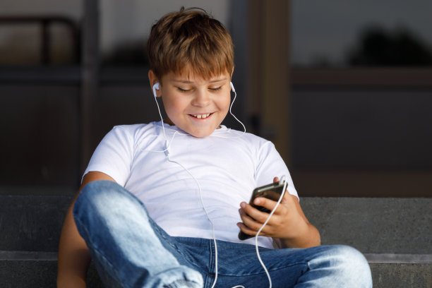 时髦男孩戴着耳机和智能手机在公园里听音乐图片下载