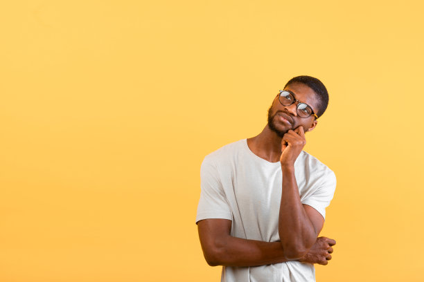 好的报价。一名戴着眼镜的沉思黑人抬头望着复印空间，在黄色的画室背景上摸着下巴图片下载
