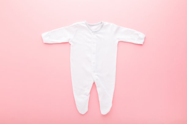 白色婴儿睡衣与长胳膊和腿浅粉色的桌子背景。柔和的颜色。特写镜头。自顶向下的观点。图片下载