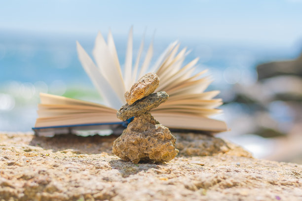 一个由小石块组成的金字塔和一本以大海为背景的打开的书图片下载