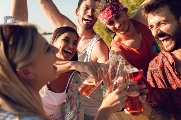 年轻的朋友们站在码头上喝着酒精饮料，在湖边享受夏日图片下载