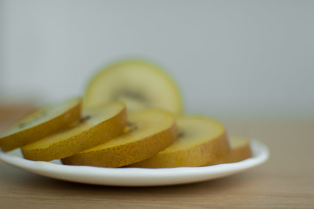 厨房的白色盘子上放着金黄色果肉的几片猕猴桃。异域水果，健康饮食理念图片下载