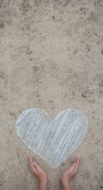 白色的心画用粉笔画在街道的地板上，用两个孩子的手拿着保护、世界和平、环保理念的垂直横幅用复制空间。图片下载