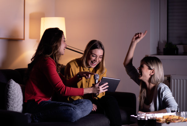 三个女性朋友坐在沙发上玩卡拉ok在家。图片下载