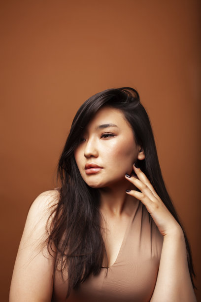 年轻漂亮的亚洲女人愉快的微笑在温暖的棕色背景，生活方式的人的概念图片下载