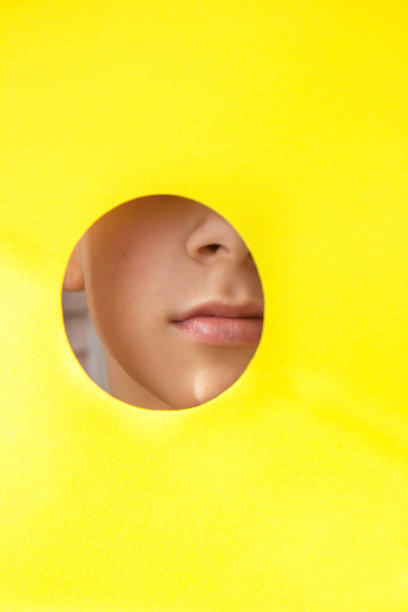 一张美丽的女孩的脸从黄色的纸洞里向外窥视图片下载