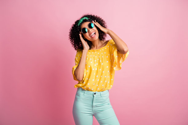 照片上的年轻漂亮的女人喜欢音乐，唱歌，穿绿色的裤子，裤子隔离在粉红色的背景图片下载