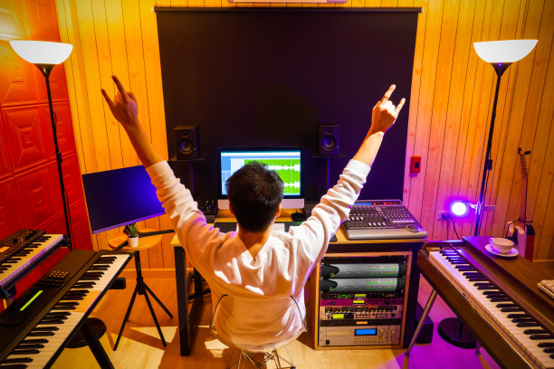 背部的亚洲男性音乐制作人显示摇滚手势，而享受听他的歌曲在家庭录音室图片下载