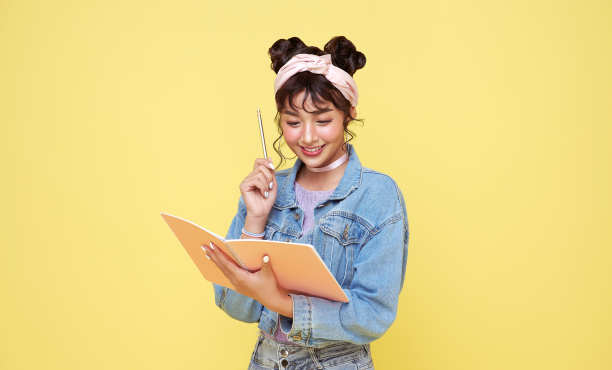 快乐的亚洲女孩拿着铅笔和笔记本在黄色的背景。回到学校的概念。图片下载