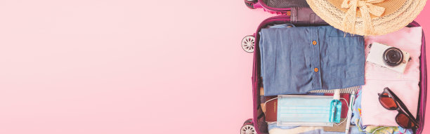 粉色背景上有衣服和面具的旅行袋。新冠肺炎疫情下的暑期旅游。网络横幅的尺寸。图片下载