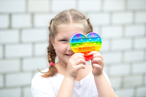 画一个小女孩和一个心形的现代波普特玩具。色彩鲜艳的pop it玩具简单的酒窝。时尚的抗压力感官玩具烦躁推pop它和简单的酒窝在孩子的手中图片下载