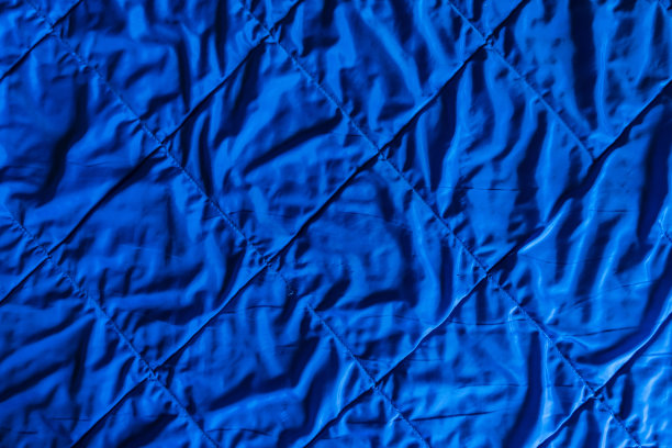 一张旧被子表面的特写。闪亮的蓝色织物用装饰性的方线缝制。表面有轻微的皱纹。背景。纹理。图片下载
