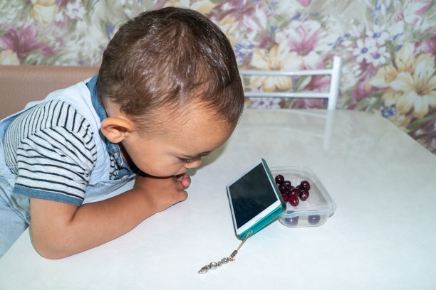 小男孩在餐桌边吃早餐，用智能手机看卡通片图片下载