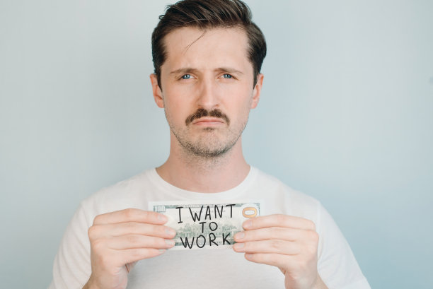 一个人手里拿着一张百元大钞，上面写着“我要工作”。失业、收入下降、工资低的概念图片下载