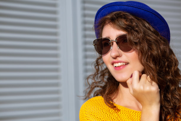 特写照片的快乐的女人戴着蓝色的帽子和黄色针织毛衣摆姿势在阳光。空的空间图片下载