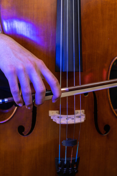 木制的大提琴带着蓝色的光，手带着音乐的弓，弹拨着琴弦，选择性的专注地演奏着一首歌图片下载