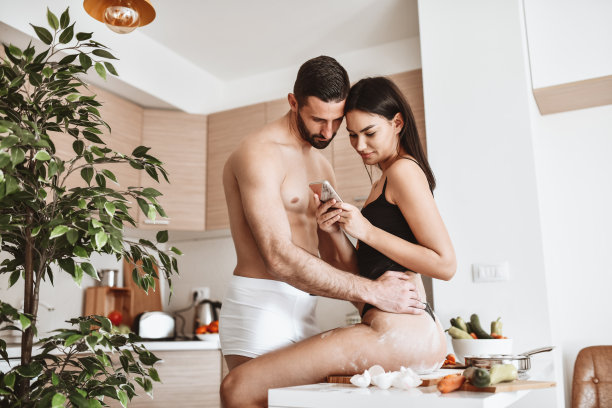 女性做完饭和男朋友看手机后坐在凌乱的厨房台上图片下载