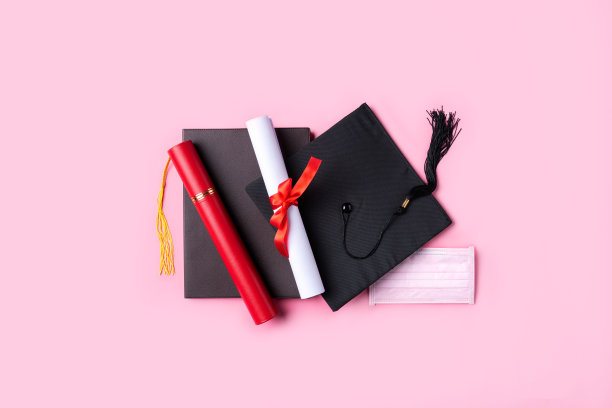 毕业学位帽与毕业文凭和面具隔离在粉红色的桌子背景上。图片下载