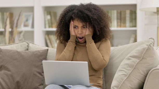 年轻的非洲妇女用笔记本电脑对沙发上的失败做出反应图片下载