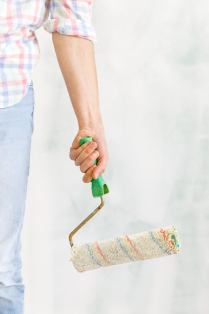 穿着便服的人/画家，拿着一个脏滚筒在墙上作画图片下载