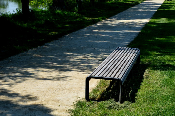 满是尘土的公园小径沿着池塘蜿蜒穿过一片草地。它通向桥，路上有长板凳和木制的木板和垃圾桶图片下载
