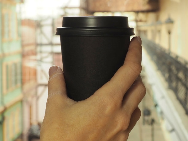 一个女人的手拿着一个装着咖啡的黑纸板玻璃杯。特写照片图片下载