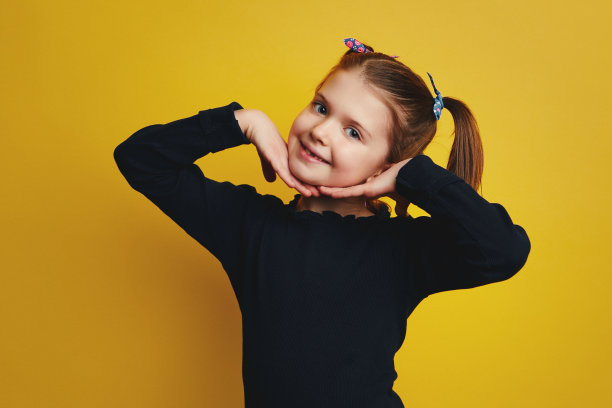 女孩牵着手在脸颊微笑的相机孤立在黄色的墙图片下载