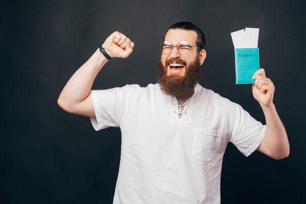 廉价航班的概念。一幅惊讶激动的大胡子男子的肖像，他拿着护照和登机牌票，站在dar的背景下。图片下载
