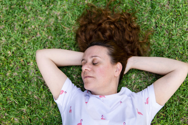 一个漂亮的白人年轻女子的肖像躺在草地上休息放松图片下载