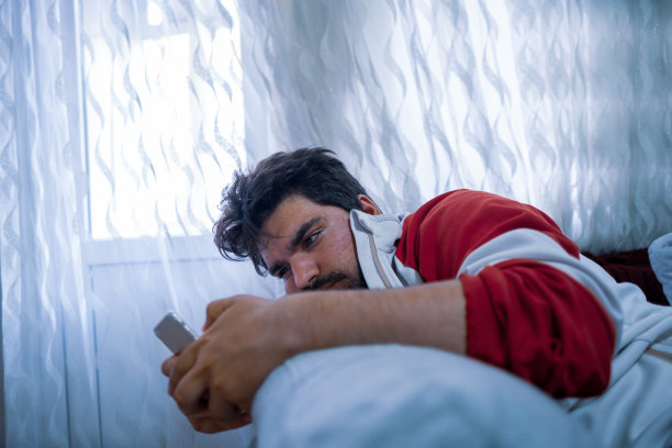 一个英俊无聊的年轻人，穿着休闲装，用智能手机上网图片下载