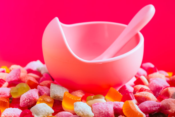 儿童餐具硅胶碗与汤匙。提供婴儿食品，儿童餐具。粉红色的硅胶碗和勺子堆在一堆糖果和果酱中。明亮的彩色照片图片下载