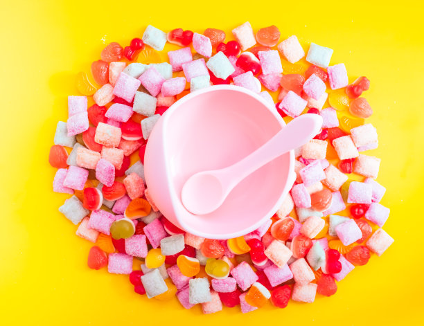 儿童餐具硅胶碗与汤匙。提供婴儿食品，儿童餐具。粉红色的硅胶碗和勺子堆在一堆糖果和果酱中。明亮，色彩斑斓的照片平淡图片下载