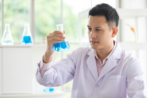 一个年轻的科学家拿着科学玻璃烧瓶和蓝色液体在一个实验室图片下载