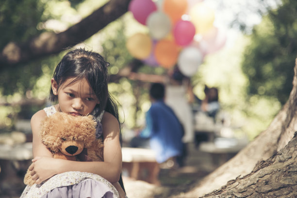 悲伤的女孩拥抱泰迪熊悲伤独自在绿色花园公园。孤独的女孩感觉伤心不快乐坐在户外与最好的朋友玩具。自闭症儿童玩泰迪熊最好的朋友。家庭暴力的概念图片下载