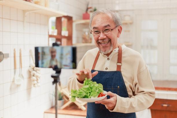 特写镜头记录了退休的成熟男子烹饪和为社交媒体平台制作视频直播。退休的网红在自家厨房里制作视频内容图片下载