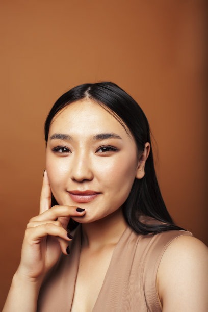 年轻漂亮的亚洲女人愉快的微笑在温暖的棕色背景，生活方式的人的概念图片下载
