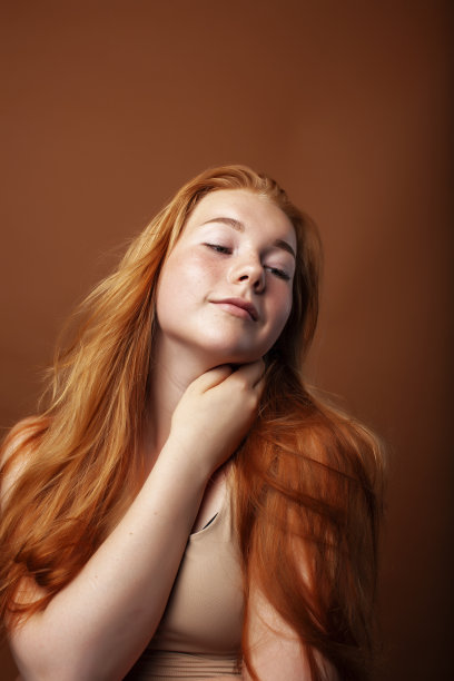 年轻漂亮的红发女孩摆出欢快的姿态在温暖的棕色背景下，生活方式的人的概念图片下载