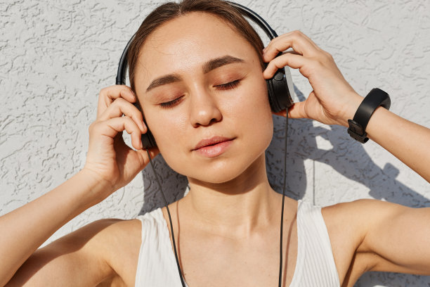 年轻的成年女性，深色头发，白色上衣，闭上眼睛，用手掌触摸耳机，在运动后享受音乐，健康的生活方式。图片下载