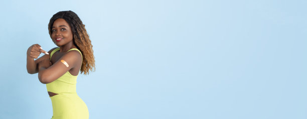 美丽的非洲裔美国年轻女子在黄色连体衣摆姿势在蓝色工作室背景图片下载
