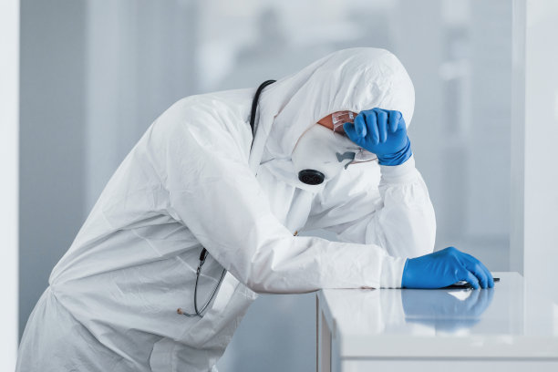 疲惫的科学家医生穿着实验服，戴着防护眼镜和口罩休息图片下载