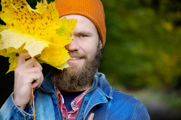 季节性的秋季时装。一个男人用秋叶遮住脸的肖像。秋天的本性。图片下载