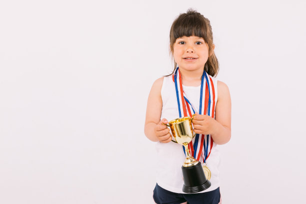 棕色头发的小女孩拿着运动冠军奖牌，双手举着奖杯。运动与胜利理念图片下载