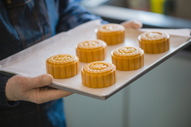 一个亚洲人拿着自制的中国月饼糕点在烤盘上准备放进烤箱烤。支持本地小型企业的理念。图片下载