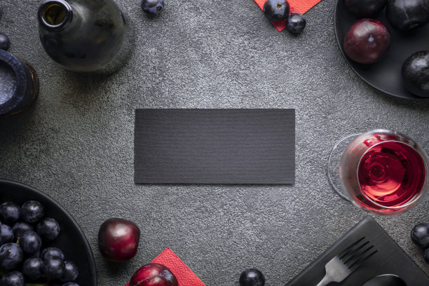 明信片是邀请人们去葡萄酒餐厅庆祝。深色概念配一瓶红酒，一杯李子和葡萄，平铺图片下载
