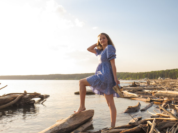 年轻美丽的赤脚女人在夏天的蓝色太阳裙在海滩上日落图片下载