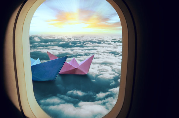 飞机窗户被看作是两艘粉红色和蓝色的船漂浮在云，太阳在背景照耀图片下载