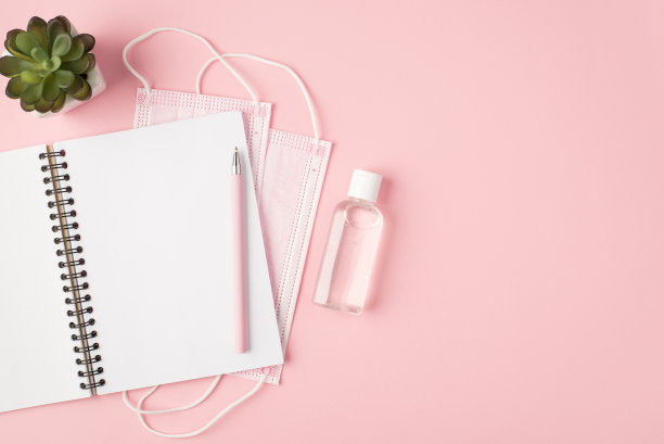俯视图照片的两个粉色医疗口罩，消毒剂，开放式计划笔和花盆在孤立的淡粉色背景与copyspace图片下载