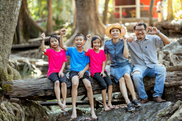 家庭和孩子们坐在自然瀑布的木材或原木上，快乐的家庭在假期放松时间，孩子们在自然瀑布中玩耍和学习，夏季亚洲家庭旅游图片下载