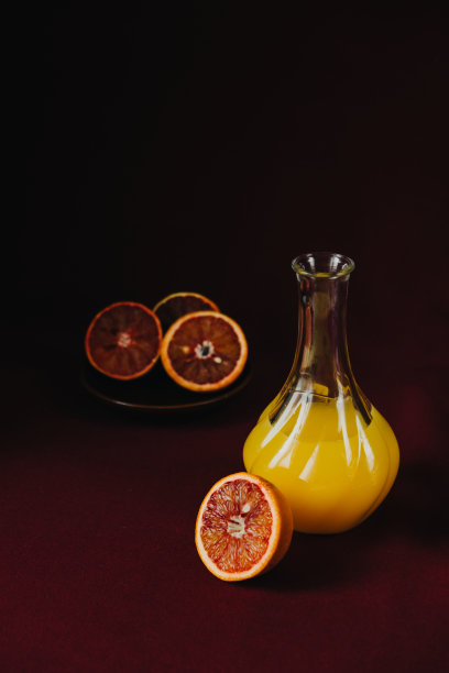 酒红色布料上的玻璃花瓶里的鲜橙汁，深色食物照片图片下载