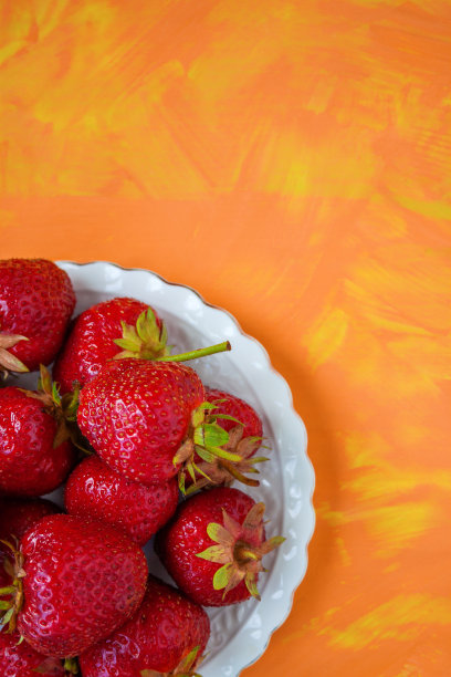 白色盘子上放着成熟的红草莓，背景是橙黄色图片下载